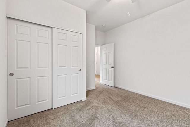 unfurnished bedroom featuring ceiling fan, a closet, light colored carpet, and a textured ceiling