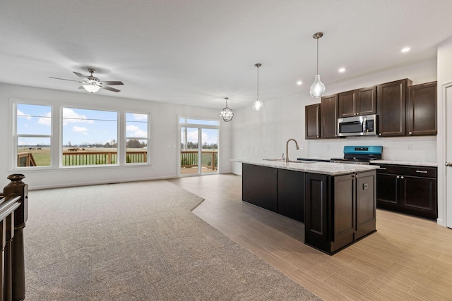 kitchen with dark brown cabinetry, stainless steel appliances, sink, pendant lighting, and an island with sink