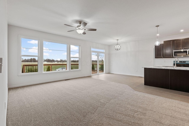 unfurnished living room featuring light colored carpet and ceiling fan with notable chandelier