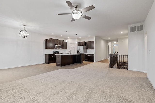 kitchen featuring light carpet, a center island with sink, hanging light fixtures, appliances with stainless steel finishes, and dark brown cabinets