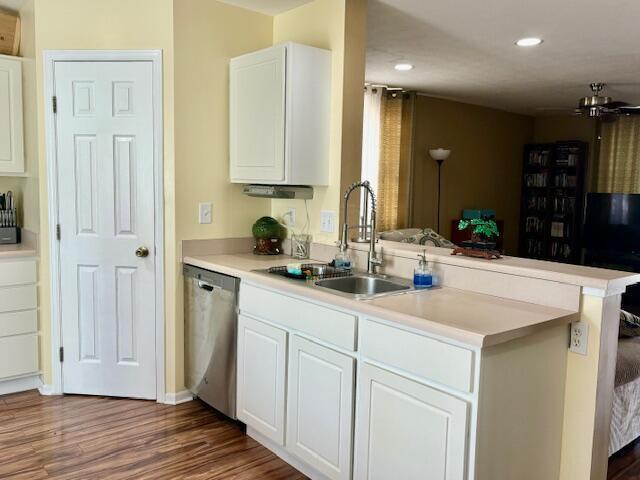 kitchen with kitchen peninsula, dark hardwood / wood-style flooring, stainless steel dishwasher, sink, and white cabinets