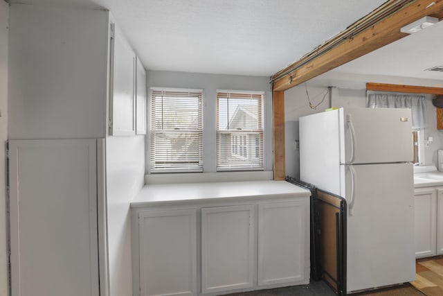 kitchen with white fridge, white cabinetry, and a textured ceiling