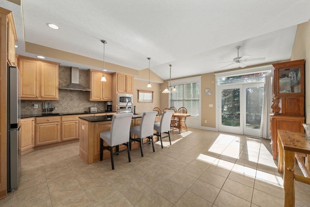 kitchen featuring a center island with sink, wall chimney range hood, decorative backsplash, appliances with stainless steel finishes, and decorative light fixtures