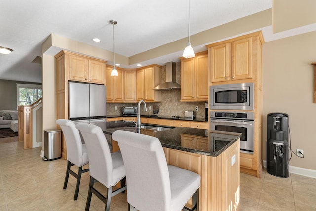 kitchen with wall chimney exhaust hood, an island with sink, decorative light fixtures, and appliances with stainless steel finishes