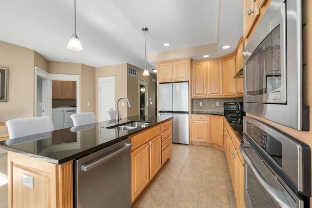 kitchen featuring washing machine and clothes dryer, sink, stainless steel appliances, decorative light fixtures, and a center island with sink