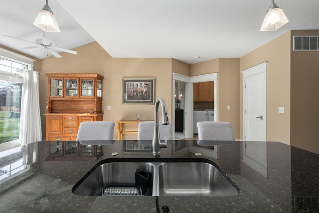 kitchen featuring dark stone countertops, sink, decorative light fixtures, and washing machine and dryer