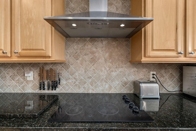 kitchen with backsplash, black electric cooktop, wall chimney exhaust hood, and dark stone counters