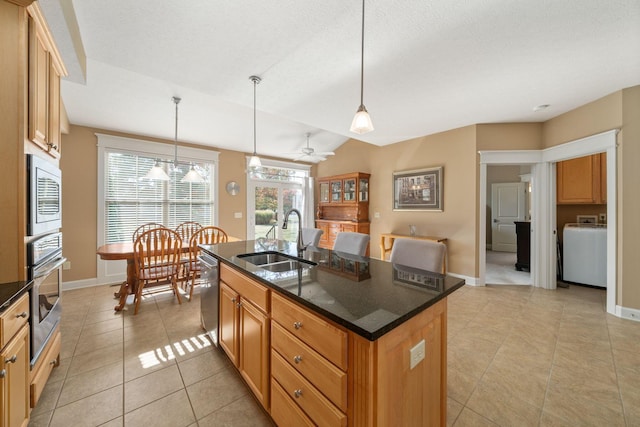 kitchen with sink, decorative light fixtures, washer / dryer, a kitchen island with sink, and appliances with stainless steel finishes