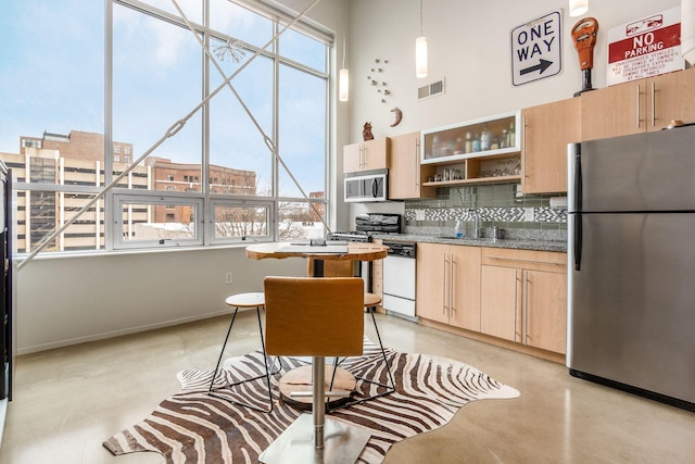 kitchen with appliances with stainless steel finishes, light brown cabinetry, tasteful backsplash, sink, and decorative light fixtures