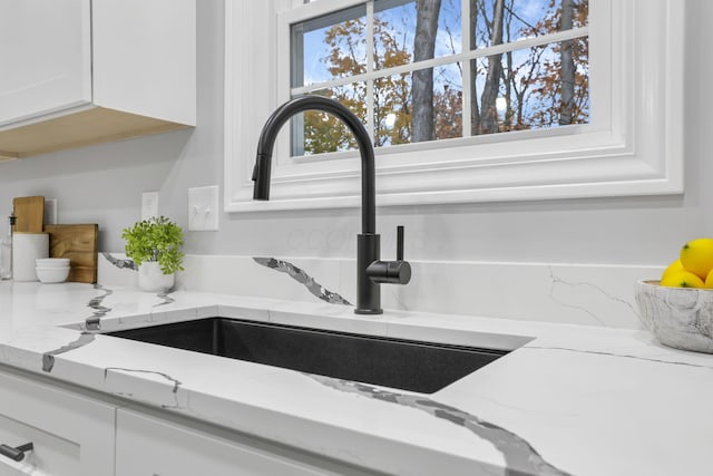 details featuring white cabinets, light stone countertops, and sink