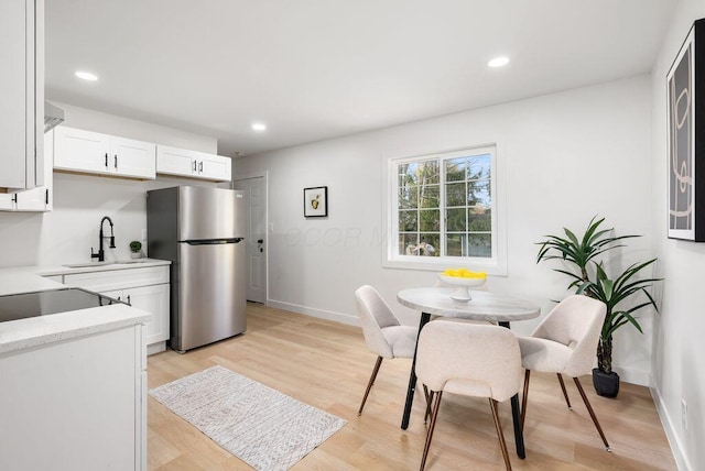 kitchen featuring stainless steel refrigerator, white cabinetry, sink, and light hardwood / wood-style floors