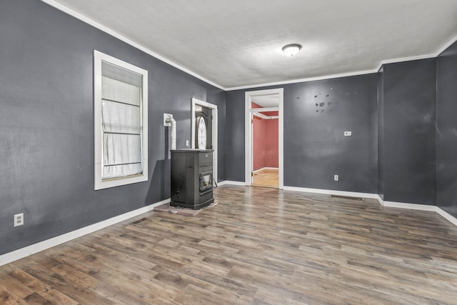 unfurnished room featuring a textured ceiling, hardwood / wood-style flooring, a wood stove, and crown molding