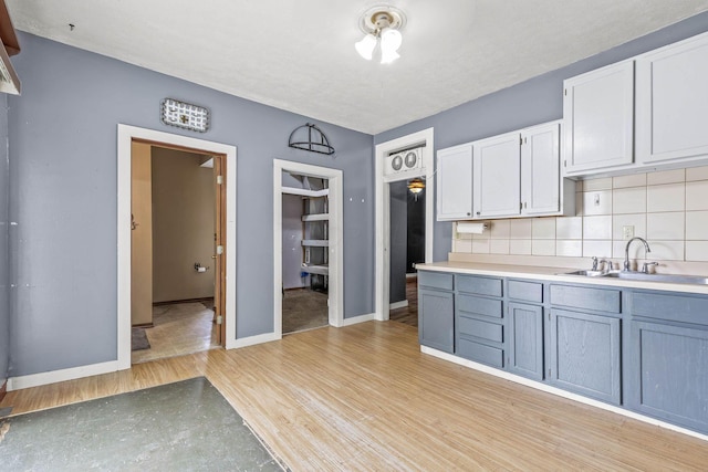 kitchen with white cabinets, light wood-type flooring, tasteful backsplash, and sink