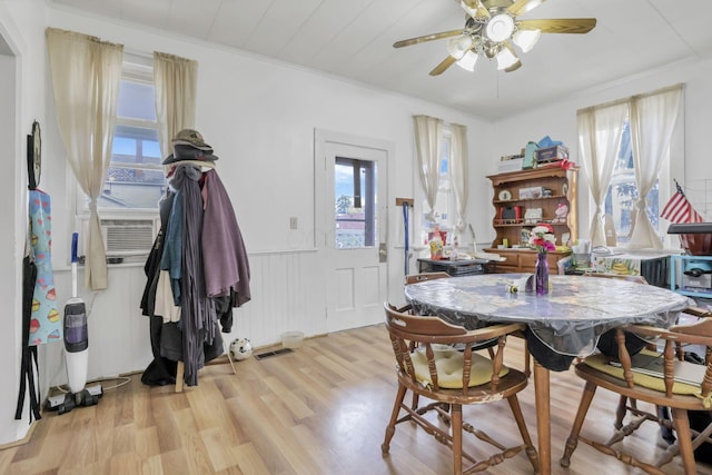 dining area with visible vents, light wood-style floors, a ceiling fan, wainscoting, and cooling unit