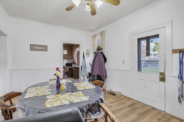 dining room featuring a ceiling fan, a wainscoted wall, crown molding, and light wood finished floors