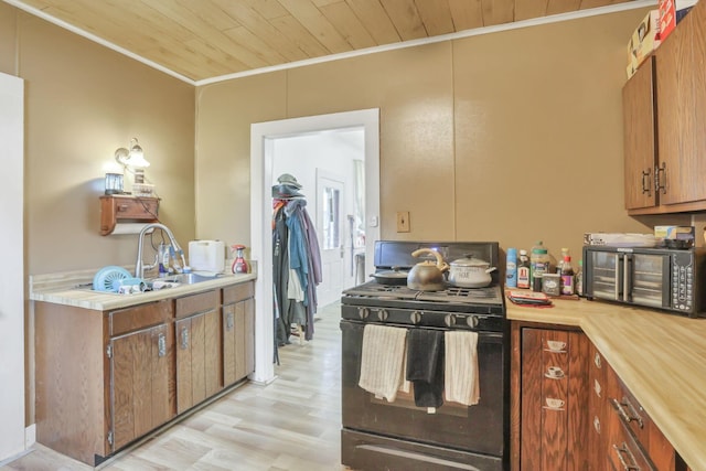 kitchen with a sink, wood ceiling, light countertops, ornamental molding, and black gas range oven