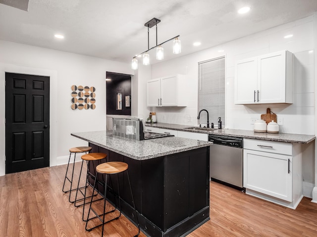 1327 Atcheson St, Columbus, OH 43203 - kitchen with stainless steel dishwasher, a kitchen bar, a kitchen island, light stone countertops, and white cabinets