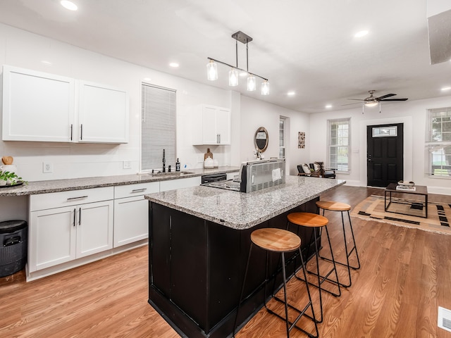 1327 Atcheson St, Columbus, OH 43203 - kitchen with light wood-style floors, light stone counters, white cabinetry, a breakfast bar area, and a kitchen island