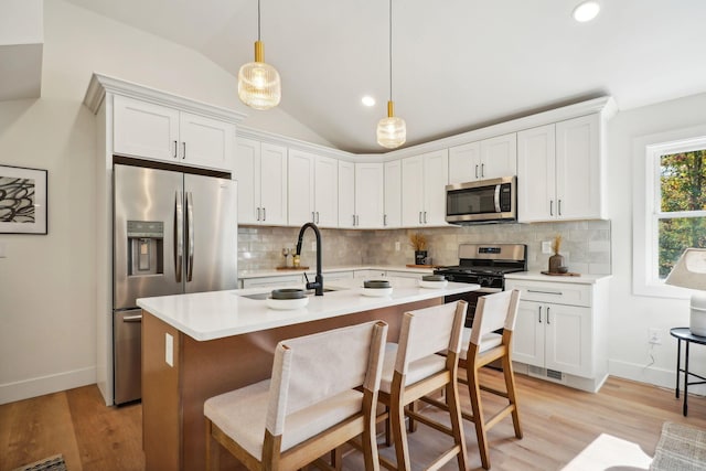 kitchen featuring backsplash, decorative light fixtures, lofted ceiling, white cabinets, and appliances with stainless steel finishes