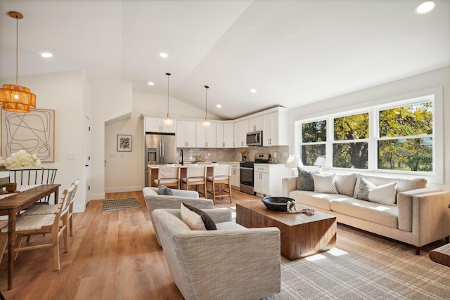 living room featuring light wood-type flooring, vaulted ceiling, and sink