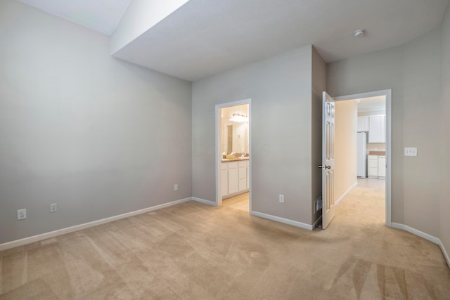 unfurnished bedroom featuring white fridge, light carpet, and connected bathroom