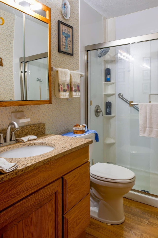 bathroom featuring vanity, a textured ceiling, a shower with door, wood-type flooring, and toilet