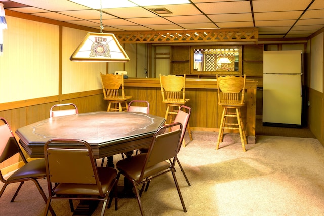 carpeted dining area featuring bar area, a paneled ceiling, and wooden walls