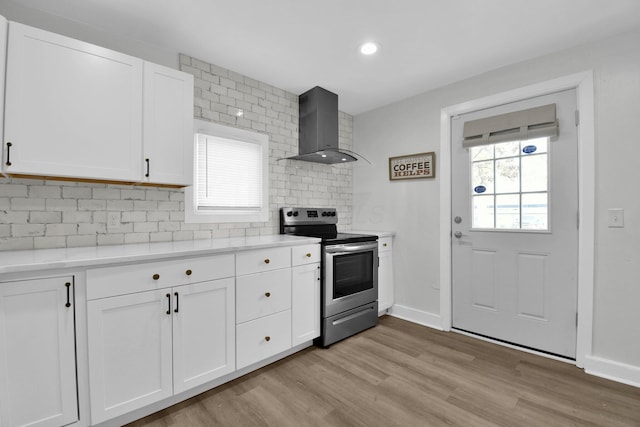 kitchen featuring plenty of natural light, white cabinetry, wall chimney range hood, and electric stove