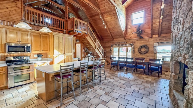 kitchen with stainless steel appliances, wooden walls, high vaulted ceiling, wooden ceiling, and hanging light fixtures