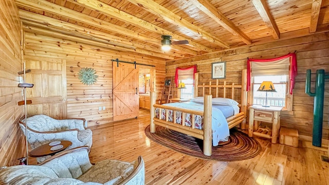 bedroom with a barn door, wooden walls, beamed ceiling, and hardwood / wood-style flooring