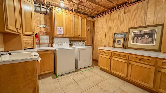 laundry room with washing machine and clothes dryer, sink, cabinets, wooden walls, and light tile patterned floors