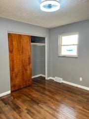 unfurnished bedroom with a barn door, a closet, and dark wood-type flooring