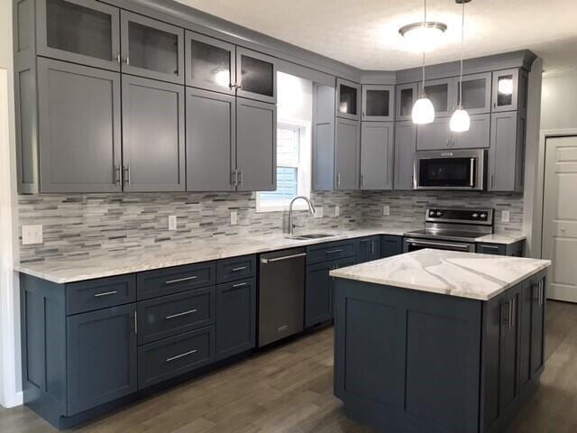 kitchen with light stone countertops, stainless steel appliances, sink, pendant lighting, and dark hardwood / wood-style floors