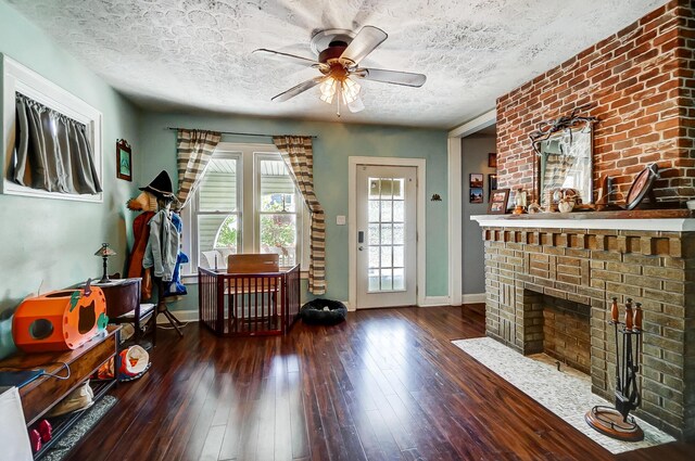 unfurnished living room featuring ceiling fan, a fireplace, dark hardwood / wood-style floors, and a textured ceiling