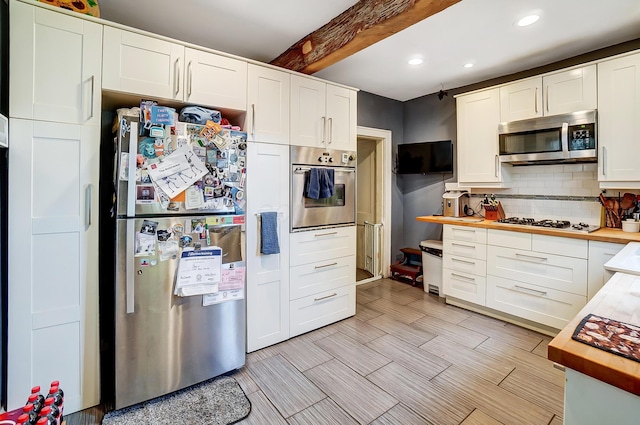 kitchen featuring butcher block countertops, white cabinetry, beamed ceiling, and appliances with stainless steel finishes