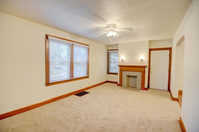 unfurnished living room featuring a tile fireplace, a textured ceiling, light colored carpet, and ceiling fan