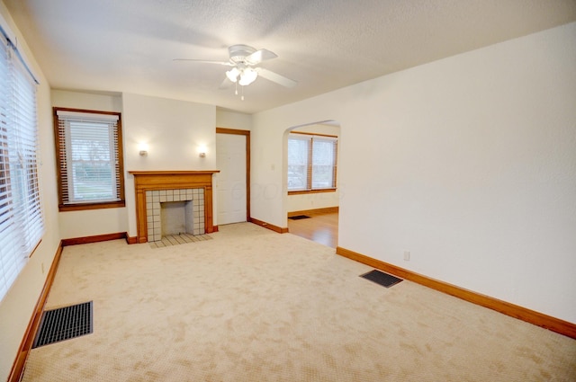 unfurnished living room with a textured ceiling, light colored carpet, ceiling fan, and a tiled fireplace