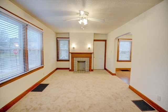 living room featuring ceiling fan, light colored carpet, a wealth of natural light, and a tiled fireplace