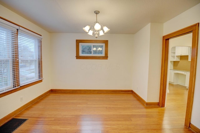 spare room with light hardwood / wood-style floors and a notable chandelier