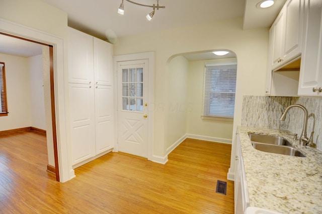 kitchen with light stone countertops, sink, white cabinets, and light wood-type flooring