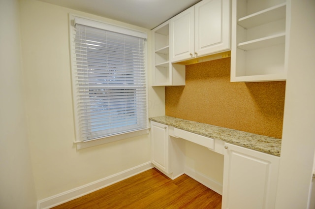 kitchen featuring white cabinets, light hardwood / wood-style flooring, decorative backsplash, built in desk, and light stone counters