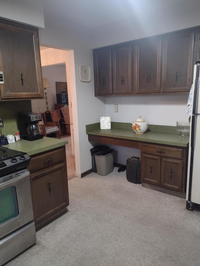 kitchen with white fridge, light colored carpet, stainless steel range with electric stovetop, dark brown cabinets, and built in desk