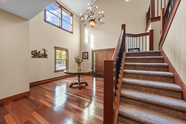 stairs with hardwood / wood-style flooring, high vaulted ceiling, and a notable chandelier