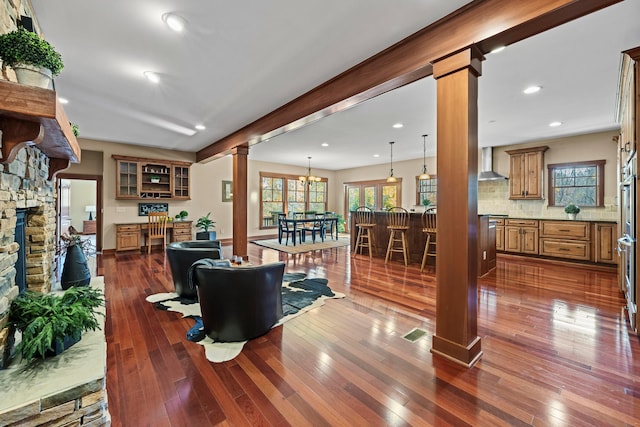 living room with decorative columns, a stone fireplace, and dark wood-type flooring