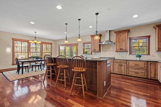 kitchen with a breakfast bar, a kitchen island, dark wood-type flooring, and wall chimney range hood