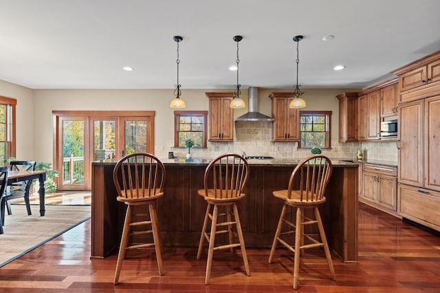 kitchen featuring a breakfast bar area, dark stone countertops, dark hardwood / wood-style flooring, and wall chimney range hood