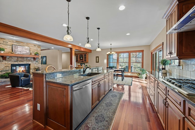 kitchen featuring sink, wall chimney exhaust hood, stainless steel appliances, pendant lighting, and a center island with sink