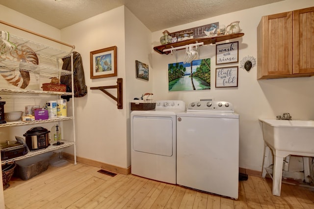 laundry area with cabinets, a textured ceiling, light hardwood / wood-style flooring, and washing machine and clothes dryer