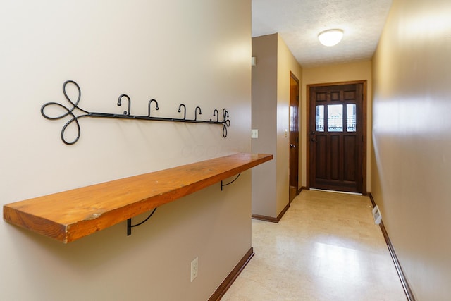 entryway featuring a textured ceiling, light floors, and baseboards