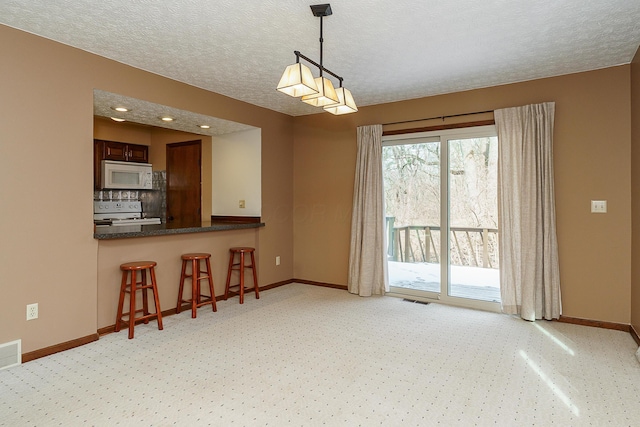 interior space featuring decorative light fixtures, dark countertops, visible vents, white appliances, and a peninsula